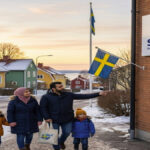 A refugee family walks toward a Migration Support Office in Stockholm, Sweden, near a Swedist sign, representing a new beginning and asylum.