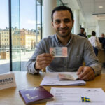 Refugee in Stockholm holding newly issued Swedish residence permit and passport, showcasing successful asylum grant and start of integration. Includes 'SWEDIST - CITIZEN GUIDES' sign.